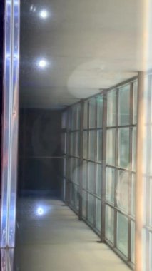 Yumuşak ve davetkar ortam aydınlatmasıyla birleştirilmiş parlak cam paneller içeren çağdaş bir koridor.