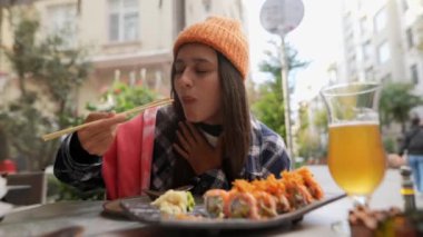 Genç bir kadın, canlı ve canlı bir açık havada yemek çubuklarıyla lezzetli suşinin tadını çıkarıyor.