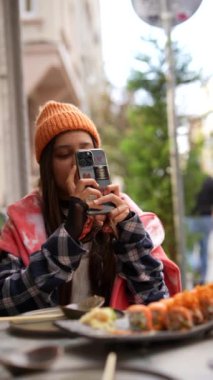 Bir kadın lezzetli suşi yemeğinin tadını çıkarırken dışarıda akıllı telefonuyla keyifli bir anı yakalıyor.