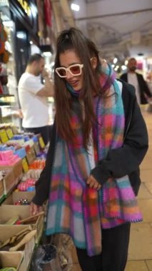 Şık bir kadın renkli ürünlerle dolu canlı bir pazarda alışveriş yapmaktan zevk alır.