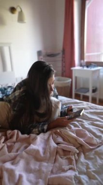 Genç bir kız rahat yatağında, akıllı telefonuna dalmış, rahat bir anın tadını çıkarıyor.