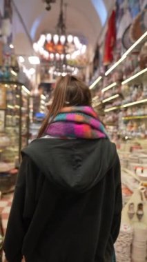 Renkli bir eşarp takmış bir insan çeşitli mallarla dolu büyüleyici ve canlı bir pazarda yürüyor.