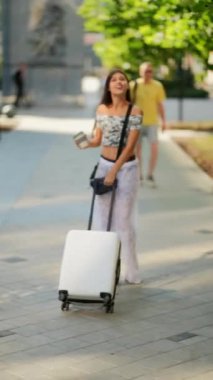 Bir kadın neşeli bir şekilde bavulunu taşırken canlı şehri keşfediyor, modern seyahat titreşimlerinin özünü somutlaştırıyor.