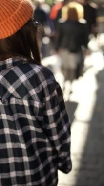 Ekose giyinmiş ve turuncu bereli şık bir figür canlı ve hayat dolu şehir manzarasının tadını çıkarıyor.