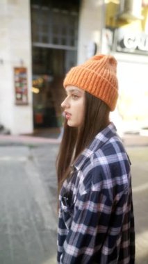 Zarif bir şekilde bereyi takan genç bir kadın canlı ve renkli bir şehir zemininin önünde düşünceli bir şekilde poz veriyor.