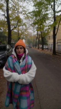 Renkli, canlı bir battaniyeye sarılmış bir kadın serin bir sonbahar gününde mutlu bir şekilde parkta dolaşıyor.