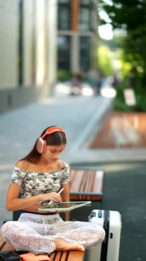 Genç bir kız bankta oturuyor, derinden müziğe dalmış, renkli, canlı bir şehirle çevrili.