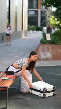 Merakla dolu genç bir kız canlı ve hareketli bir şehirde bankta otururken bavuluna bakar.