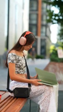 Kulaklıklı genç bir kadın, modern şehir ortamında büyüleyici bir kitaba daldı.