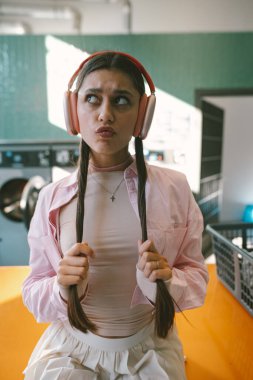 Modaya uygun bir çamaşırhanede, parlak pembe kulaklıklar takan şık genç bir kadın dikkatlice etrafına bakıyor.