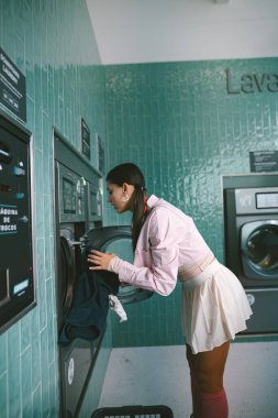 Şık bir genç kadın çamaşırlarını şık ve hareketli bir çamaşırhanede yıkıyor.