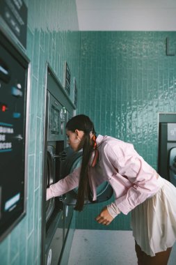 Genç bir kadın, enfes bir çamaşırhane ortamında eski bir çamaşır makinesiyle neşeyle etkileşime geçiyor.