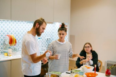 Neşeli ve canlı bir sahne, güzel tasarlanmış modern bir mutfakta birlikte yemek pişiren arkadaşları tasvir eder.