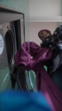 Parlak ve canlı bir çamaşırhane ortamında çamaşır makinesinin rengarenk çamaşırlarıyla uğraşan bir insan.