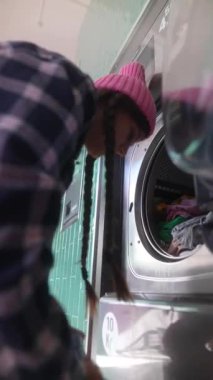 Pembe şapkalı neşeli bir çocuk neşe içinde çamaşırları katlıyor ve düzenliyor.