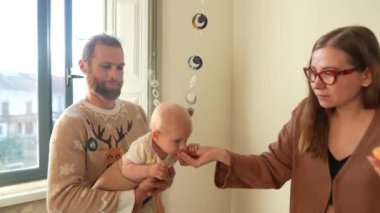 Sadık bir ebeveynin bebeğini nazikçe tutarken diğer ebeveynin sevgi dolu bir şekilde etkileşim kurduğu samimi ve dokunaklı bir sahne.