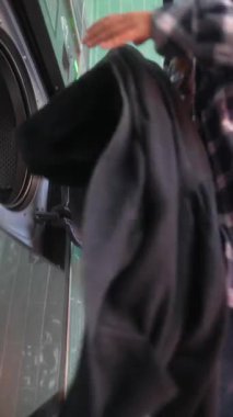 Genç bir kadın, moda bir çamaşırhanede çamaşır yıkarken modern bir çamaşır makinesine bağlanıyor.