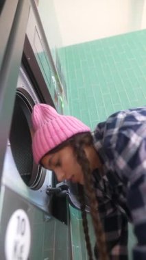 Bir kişi, şık ve çağdaş bir ortamda bulunan çamaşır makinesine çeşitli giysiler ekliyor.