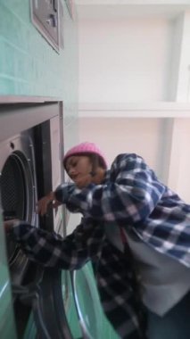 Çamaşır makinesini çalıştıran bir birey, günlük çamaşırhane işleri ile ilgili işleri aydınlatıyor.