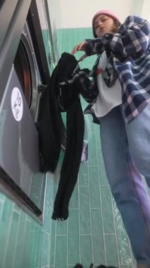 Bir kişi çamaşırhanedeki çamaşır makinesinin içinde rahat bir şekilde çamaşırlarını kontrol ediyor.