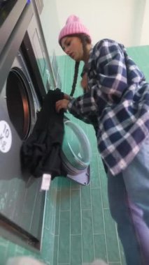 Bir kişi elbiselerini düzenli bir şekilde parlak ve iyi aydınlatılmış çamaşır makinesine yerleştiriyor. Temizlik için.