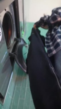 Bir birey çamaşır makinesine çeşitli giysiler koyuyor, günlük çamaşır rutinini gösteriyor.