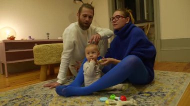 Sıcak bir aile sahnesinde, bir bebek ve iki ebeveyn keyifle sıcak ve hassas bir anı paylaşıyorlar.