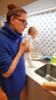 Şefkatli bir anne, bebeğini sevgiyle tutarken onları çeşitli mutfak görevlerine dahil eder, beslenme anlarını gösterir.