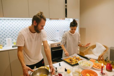 Bir çift, sıcak ve şık bir mutfakta birlikte güzel bir yemek hazırlıyor.