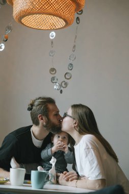 Sıcak ve rahat bir ortamda, sevgi dolu bir çift bebeklerini kucaklarken neşeyle öpüşürler.