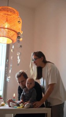 Sevecen ebeveynlerin güneşli bir yemek masasında bebekleriyle neşeyle etkileşim kurdukları sıcak ve şefkatli bir aile anı.