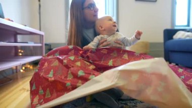 Keyifli bir ebeveyn ve neşeli bebekleri neşe içinde hediyeleri açarak neşeli bir anı paylaşıyorlar.