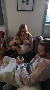 Bir anne bebeğini emzirirken, bir babanın yakınlarda oturup aile bağlarını ön plana çıkardığı samimi bir sahne..