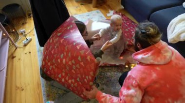 Neşeli bir aile sahnesi, neşeli bir vesileyle hediyeleri paketleme sürecinin keyfini çıkaran bir çocuğu mutlu bir şekilde yakalar.