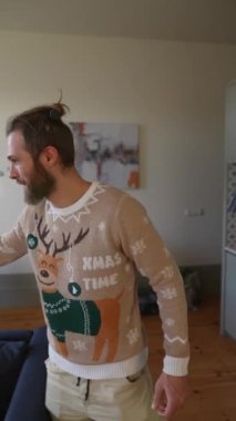 Neşeli bir adam, neşeli bir ren geyiği süveteri giyer ve sıcak, davetkar bir mutfak ortamında durur.