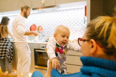 Modern bir mutfakta mutlu bir aile anı yaşanıyor. Bebek ve ebeveynler birlikte mutlu bir şekilde yemek pişiriyor.