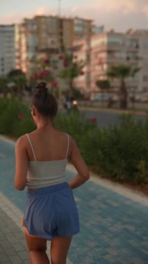 Bir kadın, güneş zarifçe batarken kentsel binaların etrafını saran pitoresk bir yolda enerjik bir şekilde koşar.
