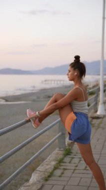 Bir kadın zarif bir şekilde kumsalda nefes kesici bir gün batımında esniyor, sağIık ve gerçek dinginliği simgeliyor.