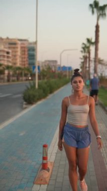 Genç bir kadın, gün batımında, yemyeşil yeşilliklerle sarılmış, güzel bir sahil yolunda güven içinde dolaşır.