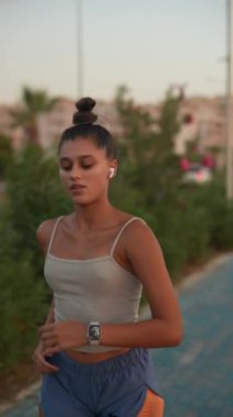 Formda ve enerjik genç bir kadın güzel bir gün batımında manzaralı bir patika boyunca koşar ve aktif yaşam tarzını gösterir.