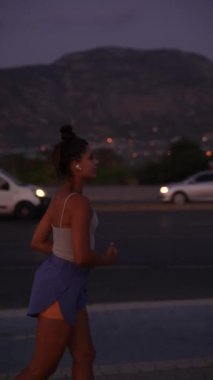 Bir kadın alacakaranlıkta kalabalık bir caddede coşkuyla koşuyor, kentsel fitness ve akşam egzersizlerini vurguluyor.