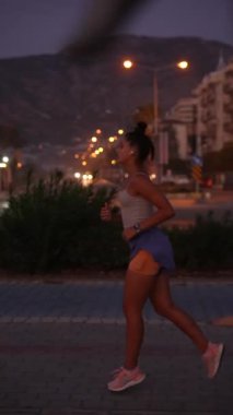 Gün batımında güzel şehir ışıklarıyla rıhtımda huzur içinde koşan bir kadın önündeki yolu aydınlatıyor.