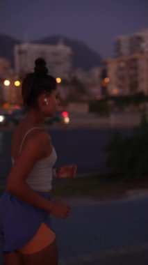 Şehir ortamında, kararlı bir kadın şehrin arka planını aydınlatan gece ışıklarıyla koşar.