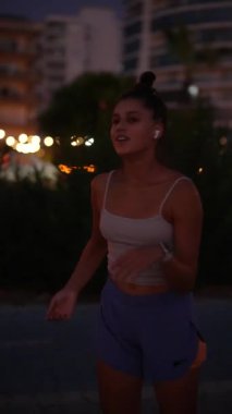 Şehir ışıkları ve hareketli hareketlerle çevrili bir kadın gece şehir ortamında enerjik bir şekilde koşuyor.