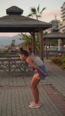 Genç bir kadın canlı ve canlı bir şehir ortamında nefes kesici bir günbatımı arkaplanına nazik bir şekilde poz verir.