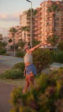 Gün batımında yoga yaparken çekilen sakin bir an. Canlı bir şehrin arka planına güzel bir şekilde kurulmuş.