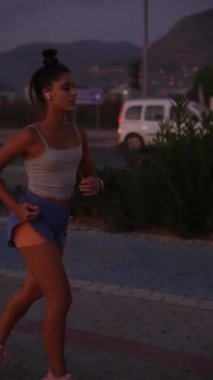 Akşam ışığında zarif bir şekilde koşan, zindelik seviyesini ve canlı şehir yaşam tarzını sergileyen bir kadın.