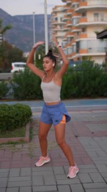 Genç bir kadın enerjik bir açık hava egzersizi yapıyor, atletik giyimde canlı aktif bir yaşam tarzını vurguluyor.