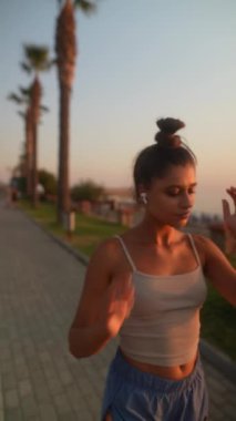 Şık, genç bir kadın güneş batarken resimli bir sahil gezintisinde rahatça geziniyor.