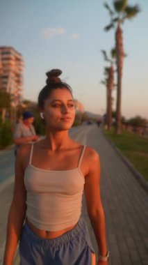 Genç bir kadın, palmiye ağaçları ve modern kentsel binaların yanında huzurlu bir akşam gezintisinden zevk alır.